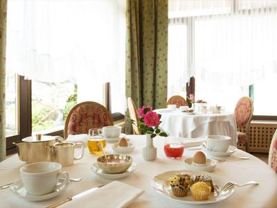 Eleganter Frühstückstisch mit Teetassen, Gebäck und Blumen vor großen Fenstern