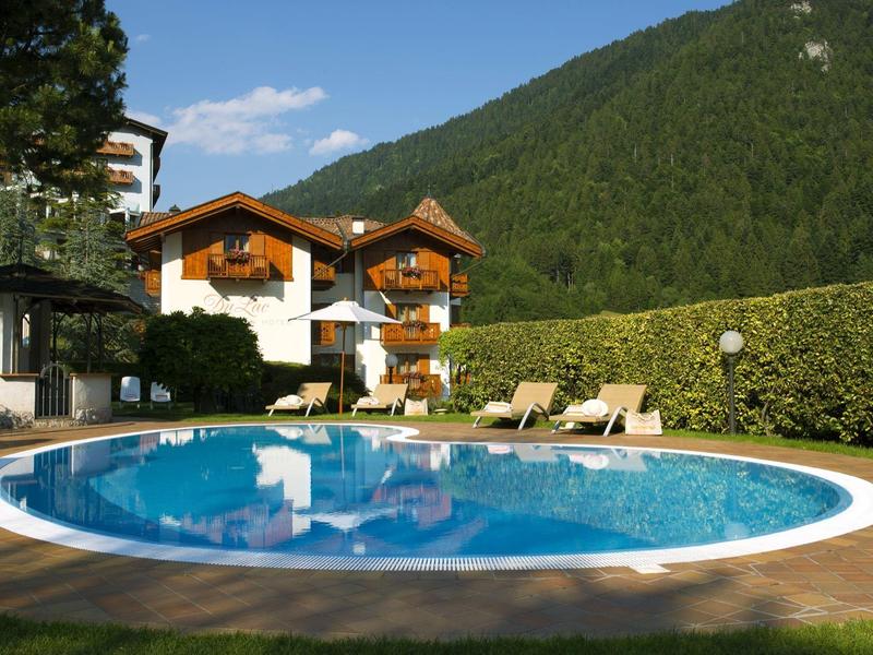 Runder Pool vor einem Hotelgebäude mit Liegestühlen und Bergen im Hintergrund.