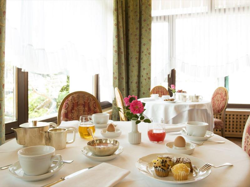 Eleganter Frühstückstisch mit Teetassen, Gebäck und Blumen vor großen Fenstern