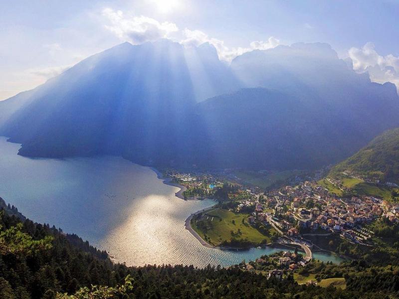 Blick auf einen See umgeben von Bergen bei Sonnenlicht mit einem kleinen Dorf am Ufer.