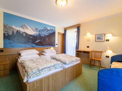 Bright hotel room with double bed, mountain picture on wall, and wooden furniture.