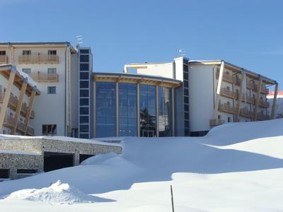 Modernes Hotelgebäude mit großen Glasfenstern, umgeben von Schnee unter klarem blauem Himmel.
