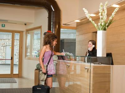 Eine Frau checkt an der Hotelrezeption ein, mit Rollkoffer und Rucksack.