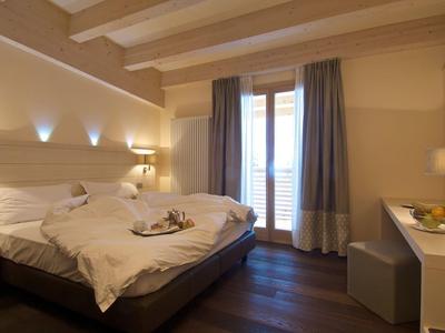 Gemütliches Hotelzimmer mit Doppelbett, Holzboden und großen Fenstern mit Gardinen.