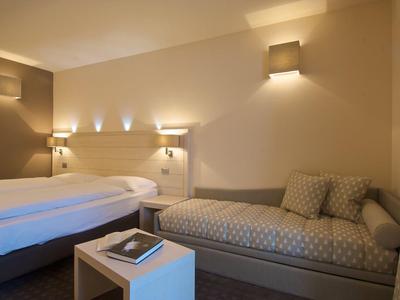 Schlafzimmer mit zwei Betten, Couch, Nachttisch und warmer Beleuchtung.