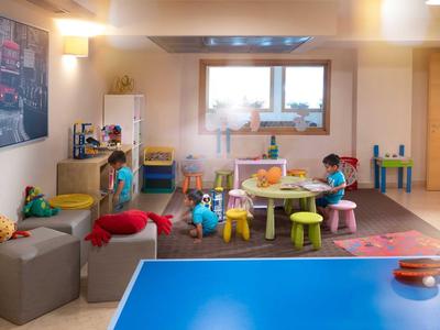 Kinderspielzimmer mit bunten Möbeln, Spielzeugen und einem blauen Tisch im Vordergrund.