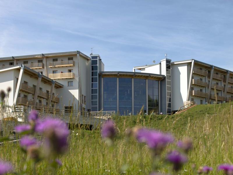 Modernes Hotel mit großen Fensterfronten und grasbewachsenem Hügel im Vordergrund