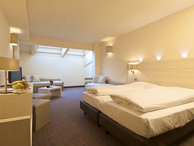 Helles Hotelzimmer mit großem Bett, Sitzbereich und moderner Beleuchtung.