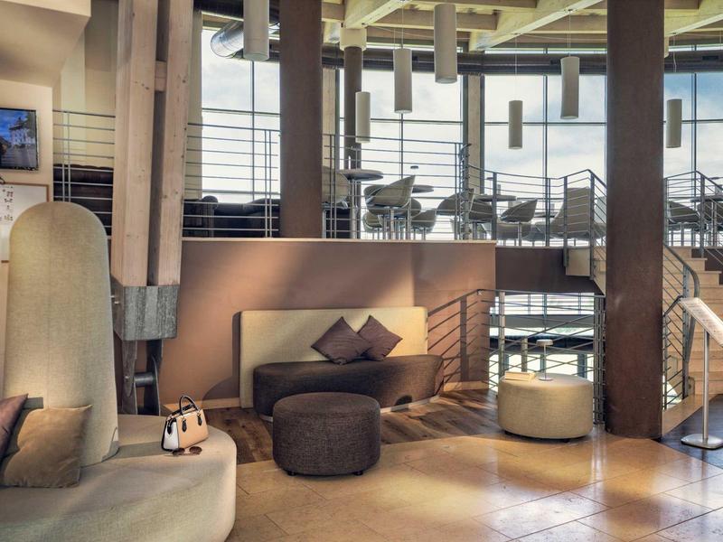 Modern gestalteter Hotel-Loungebereich mit Sesseln, Teppichen und großem Fensterfront.