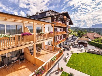 Großes Holzhaus mit Balkonen, Blumen und einer grünen Rasenfläche bei sonnigem Himmel.