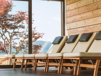 Reihen von Holzliegen mit Polstern vor großen Fenstern und Blick auf rote Bäume.