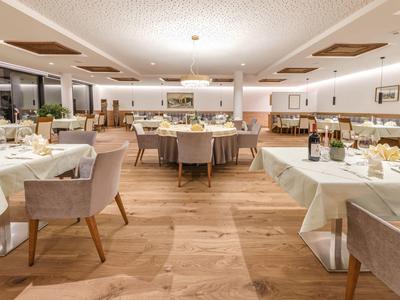 Großer heller Speisesaal mit Holzboden, weißen Tischtüchern und bequemen gepolsterten Stühlen.