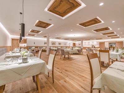 Eleganter Speisesaal mit Holzboden, weißen Tischdecken und kunstvollen Deckenelementen.