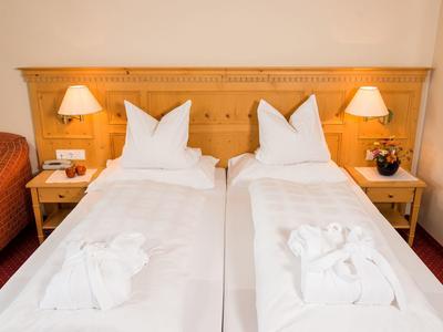 Zwei Einzelbetten mit weißen Bettdecken und Handtuch-Tieren, Holzkopfteil, Nachttische mit Lampen.