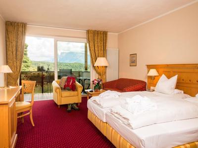 Gemütliches Hotelzimmer mit Doppelbett, Sesseln, Schreibtisch und Balkon mit Blick ins Grüne.