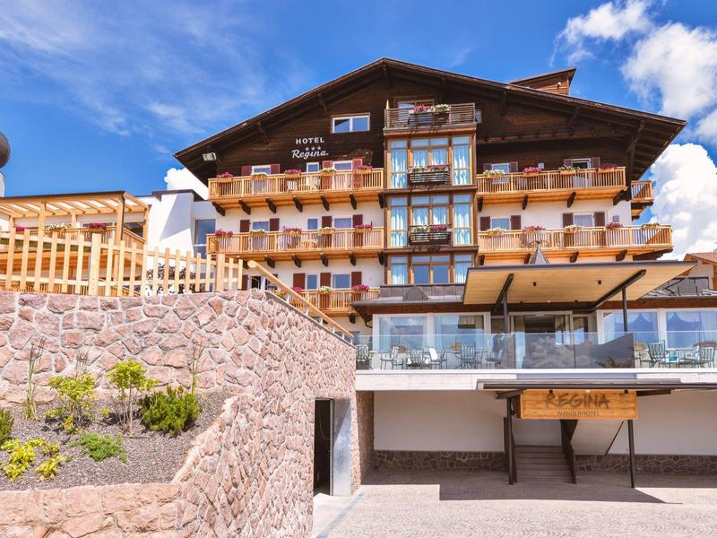 Großes Holzchalet mit Balkonen, Steinmauer und blauem Himmel im Hintergrund.
