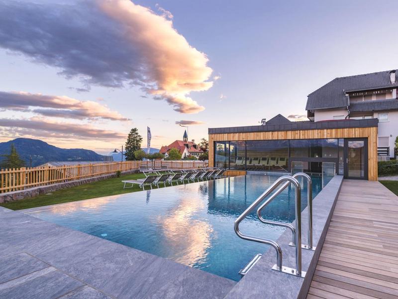 Moderner Außenpool mit Glasgeländer auf Holzdeck, Berglandschaft und Himmel mit Wolken im Hintergrund.