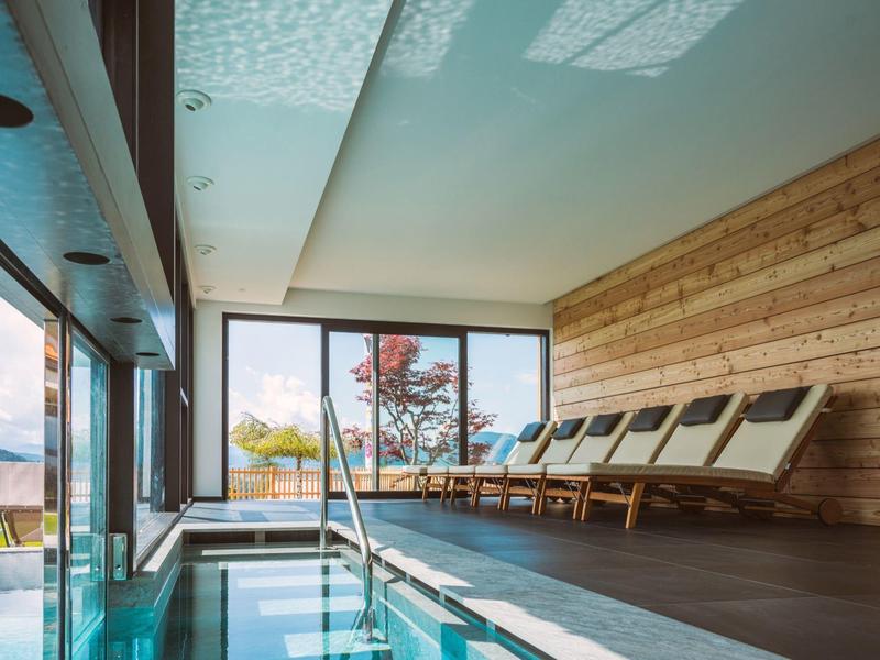 Moderner Innenpool mit Holzverkleidung, Liegestühlen, großen Fenstern und Blick ins Freie.