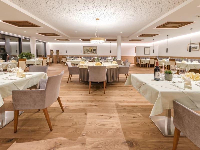 Großer heller Speisesaal mit Holzboden, weißen Tischtüchern und bequemen gepolsterten Stühlen.