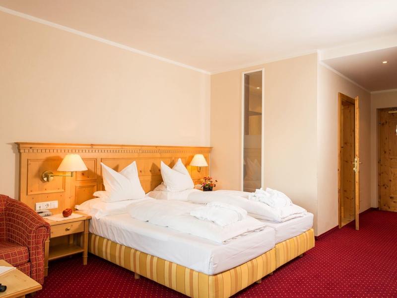 Modernes Hotelzimmer mit Doppelbett, rotem Teppich und warmen Holzmöbeln.