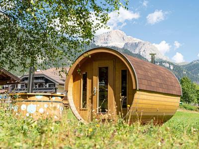 Rundes Holzhaus in grüner Wiese mit Bergen und blauem Himmel im Hintergrund.