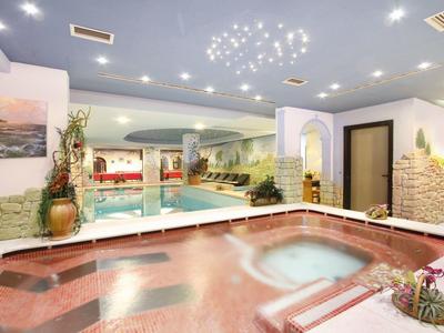 Innenraum mit Pool und Whirlpool, Wände mit Wandmalereien, helle Beleuchtung, gemütliche Atmosphäre.