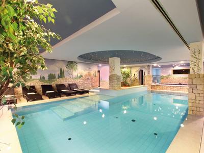 Innen-Schwimmbad mit klarem Wasser, Liegestühlen, Pflanzen und einer runden Deckenöffnung.