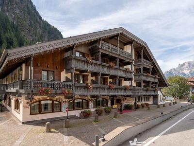 Großes, mehrstöckiges Holzhaus in alpine Landschaft mit Bergen und bewölktem Himmel im Hintergrund.