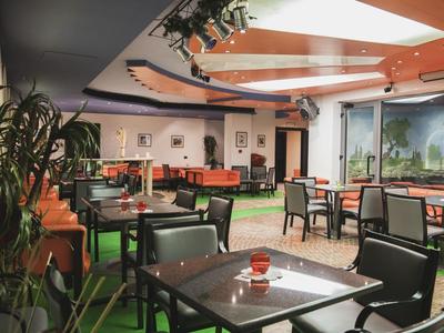 Moderne Café-Lounge mit grünen Teppichen, Holzmöbeln und großen Panoramafenstern.