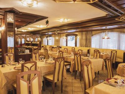 Großes Restaurant mit Holztischen, gepolsterten Stühlen und warmem, gelbem Licht.