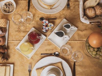 Frühstückstisch mit Brot, Brötchen, Aufstrichen, Käse, Obst und Besteck auf gelbem Tuch.