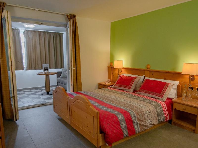 Gemütliches Schlafzimmer mit grün gestrichener Wand, Holzmöbeln und rot-grauem Bettbezug.