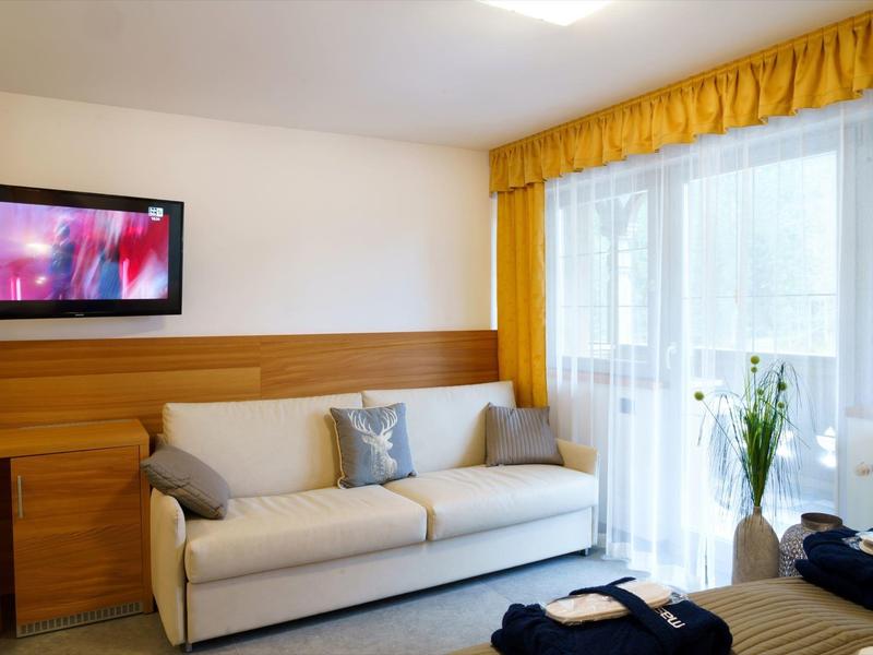 Gemütliches Wohnzimmer mit hellem Sofa, Holzwand, gelbem Vorhang und Fernseher an der Wand.