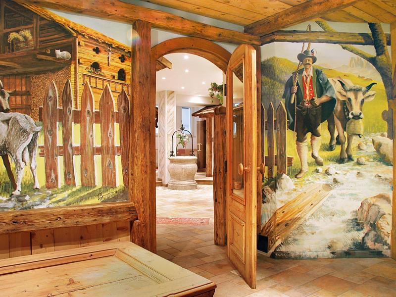 Holzraum mit bemalten Wänden, die Pferde, Reiter und Natur darstellen, und offener Holztür.