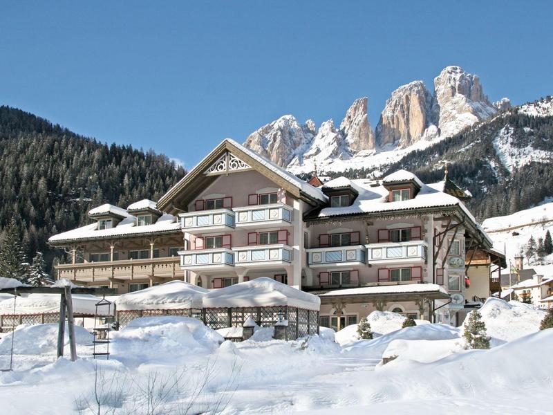 Großes Chalet aus Holz und Stein im Schnee, dahinter Tannenwald und schneebedeckte Berge.