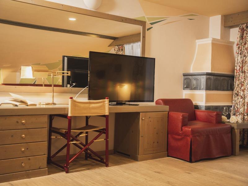 Wohnzimmer mit Schreibtisch, Fernseher, Drehstuhl, rotem Sessel, Kamin und großem Wandspiegel.