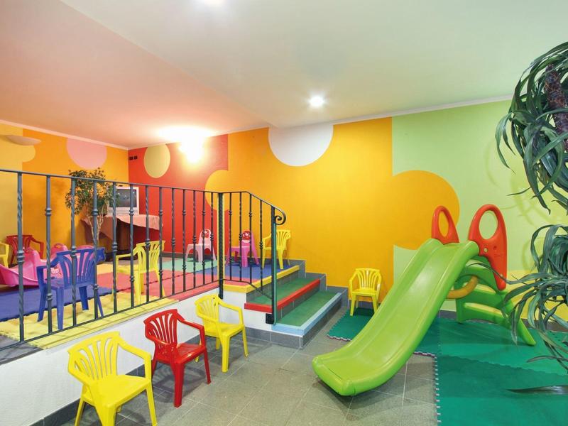 Bunte Kinderspielecke mit Rutsche, bunten Stühlen, Tisch und Treppe zur erhöhten Spielfläche.