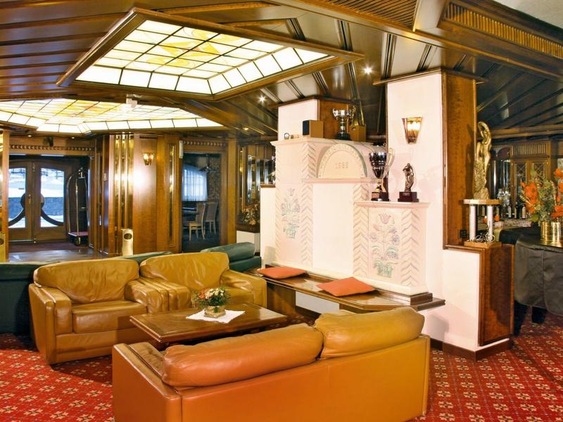 Eleganter Salon mit braunen Ledersesseln, rotem Teppich und großem Ofen in warmem Licht.