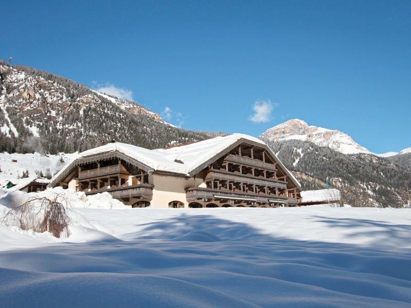 Großes Chalet mit Holzbalustraden und Schnee im Alpengebirge unter blauem Himmel.