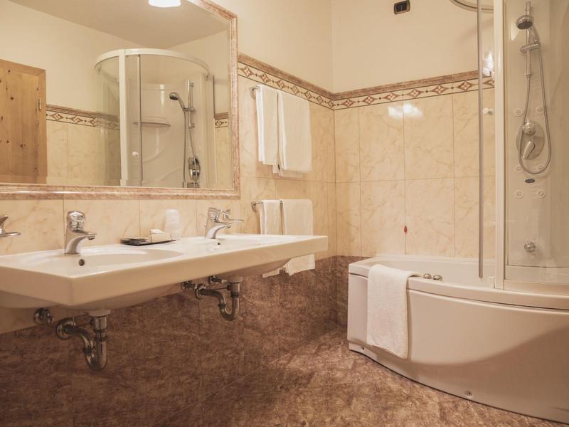 Hell beleuchtetes Badezimmer mit Doppelwaschbecken, großer Spiegel und Badewanne mit Duschkabine.