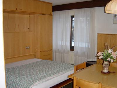 Schlafzimmer mit Holzmöbeln, Bett, grün kariertem Bettbezug, Tisch und Blumenvase.