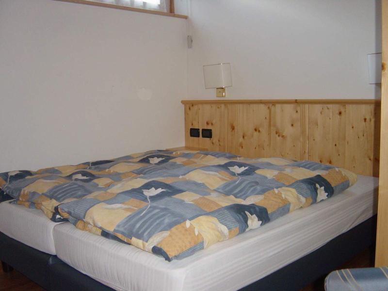 Ein einfaches Schlafzimmer mit einem Bett, einer bunten Bettdecke und einer Holzwand am Kopfende.