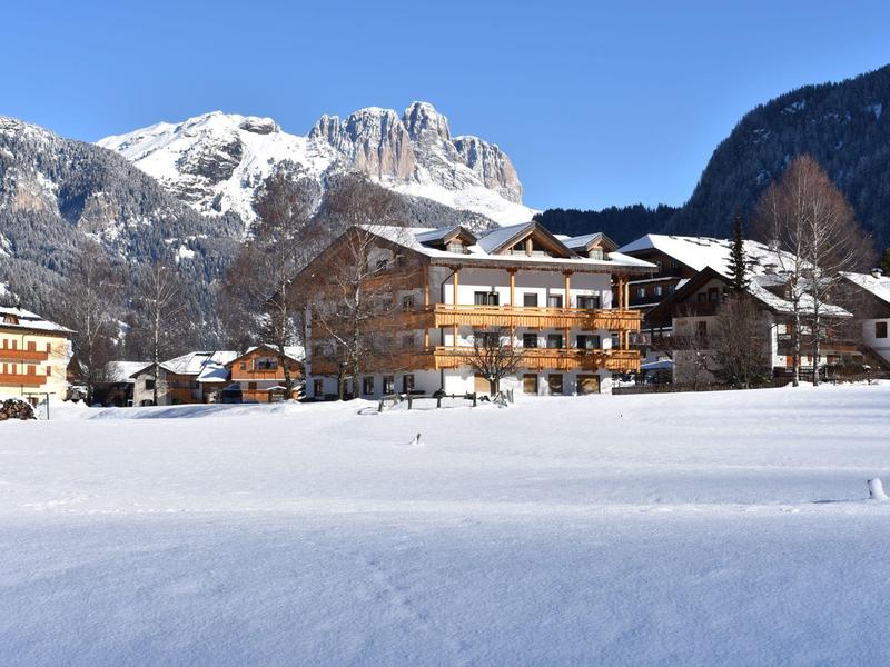 Schneebedeckte Alpenlandschaft mit traditionellen Holzhäusern unter klarem blauem Himmel.