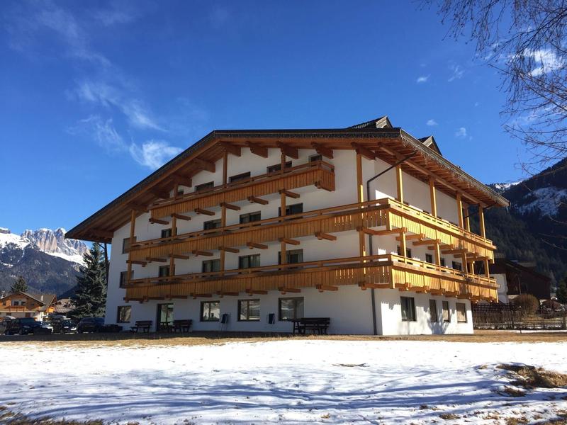 Großes Holzhaus mit Balkonen, im Schnee vor Bergen und blauem Himmel.