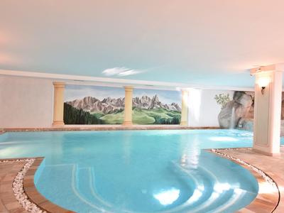 Innenpool mit runder Treppe, blauem Wasser, Holzrand und Landschaftsgemälde an der Wand.