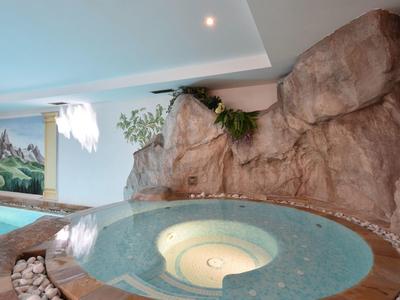 Innenwhirlpool mit blauem Wasser, umgeben von Stein-und Felswänden, mit Pflanzen und Decke.