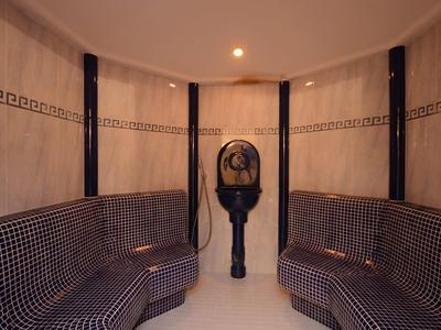 Sauna mit Mosaiksitzbänken, schwarzen Säulen und Dampfgerät in der Mitte, warmes Licht.