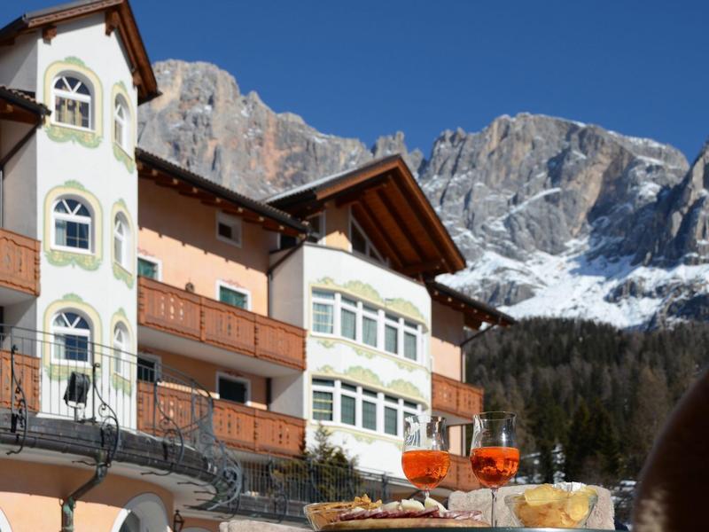 Alpenlandschaft mit einem Haus im Vordergrund, blauem Himmel und schneebedeckten Bergen im Hintergrund.