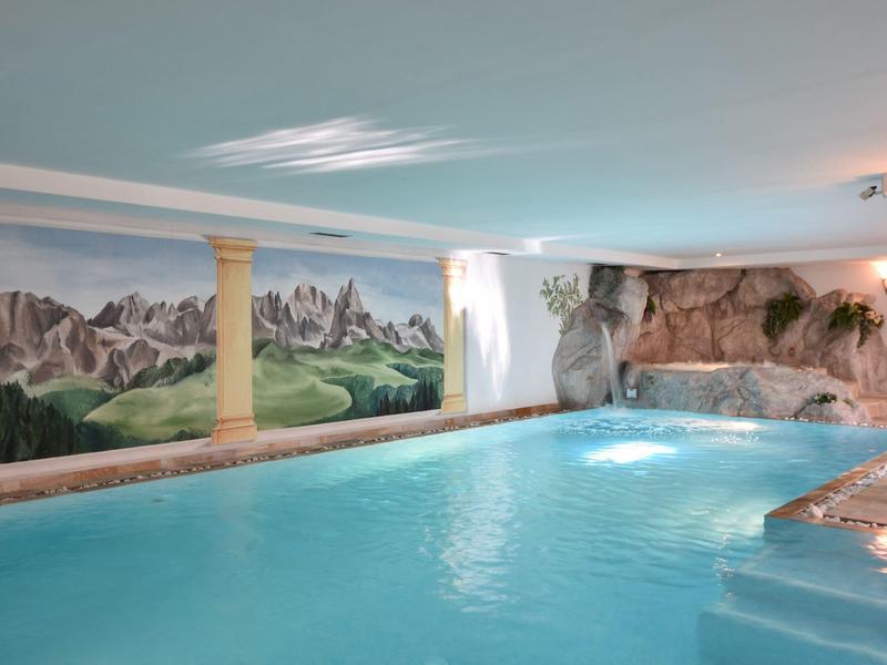 Innenraum mit großem Schwimmbad, Wandgemälde von Bergen, kunstvolle Säule und Felsen-Dekor.