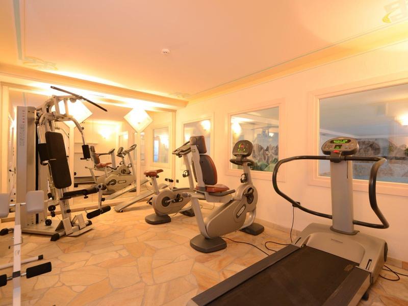 Helles Fitnessstudio mit verschiedenen Trainingsgeräten und warmem Licht in einem kleinen Raum.